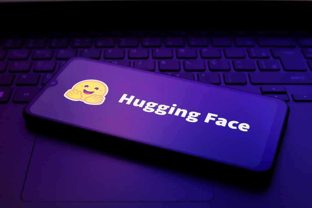 노트북 키보드 위에 놓인 스마트폰 화면에 허깅페이스(Hugging Face) 로고가 떠 있는 모습