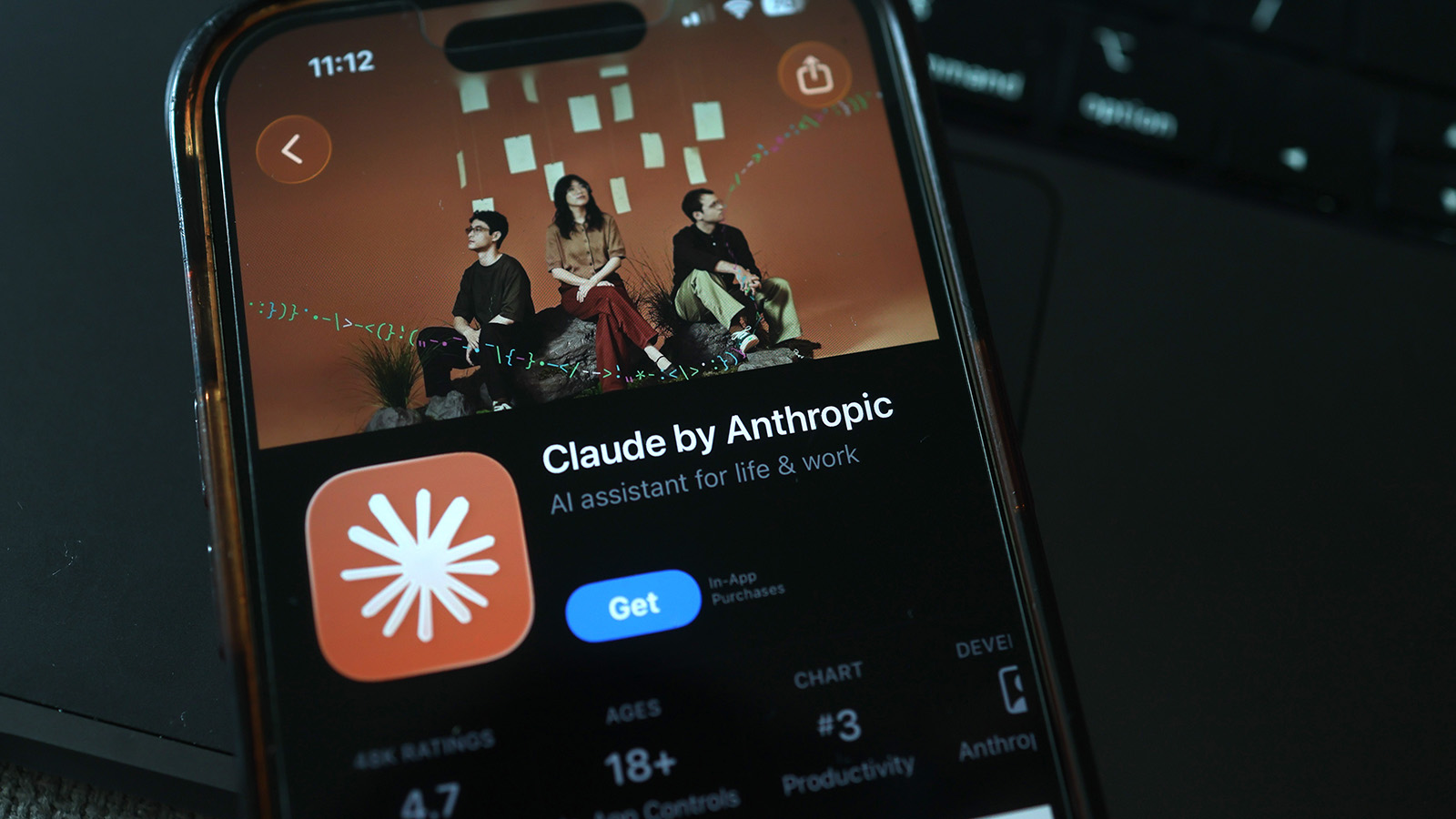 어두운 책상 위 스마트폰 화면에 떠 있는 앱스토어의 Claude by Anthropic 설치 페이지
